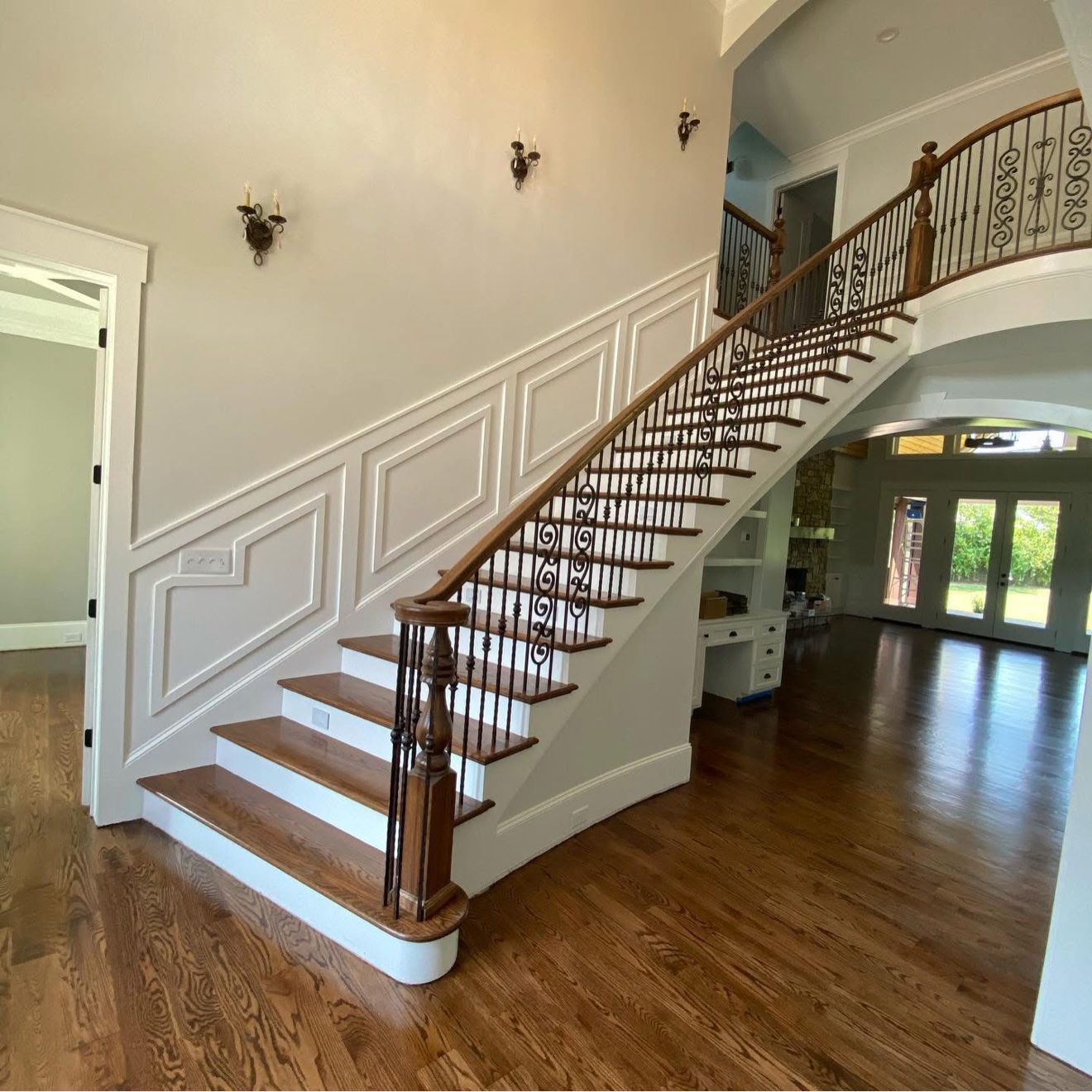 Finished hardwood foyer with a sweeping staircase, dark wood floors, iron balusters, and white wainscoting
